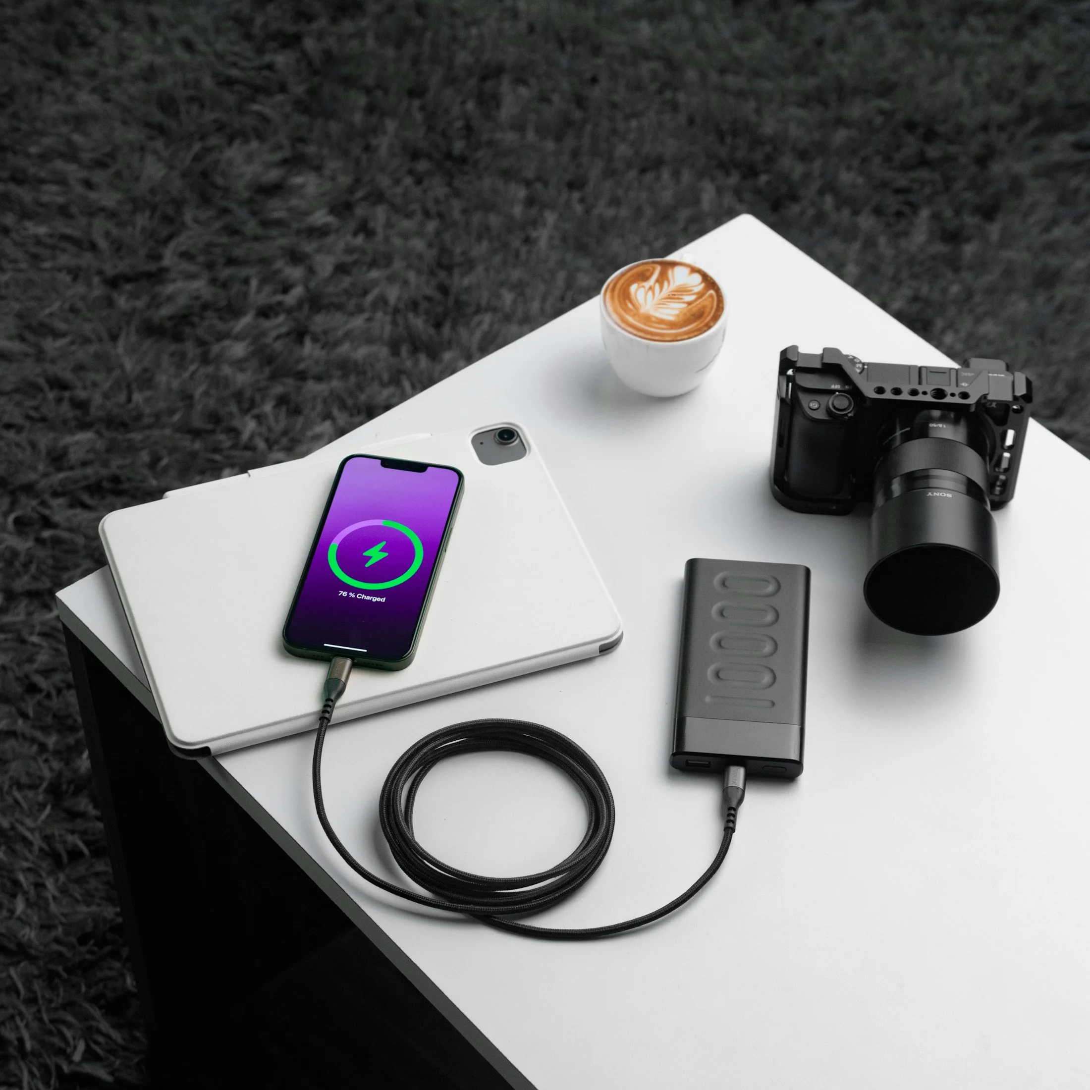 Phone, cables, a portable charging hub and camera arranged on a desk