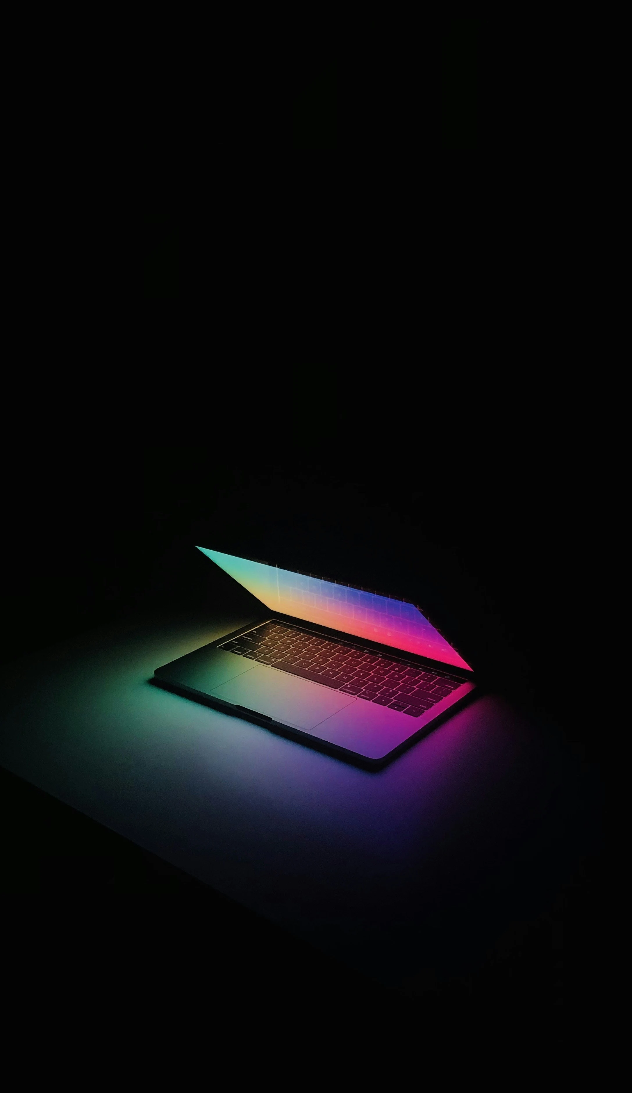 A laptop illuminated with colourful light against a black background